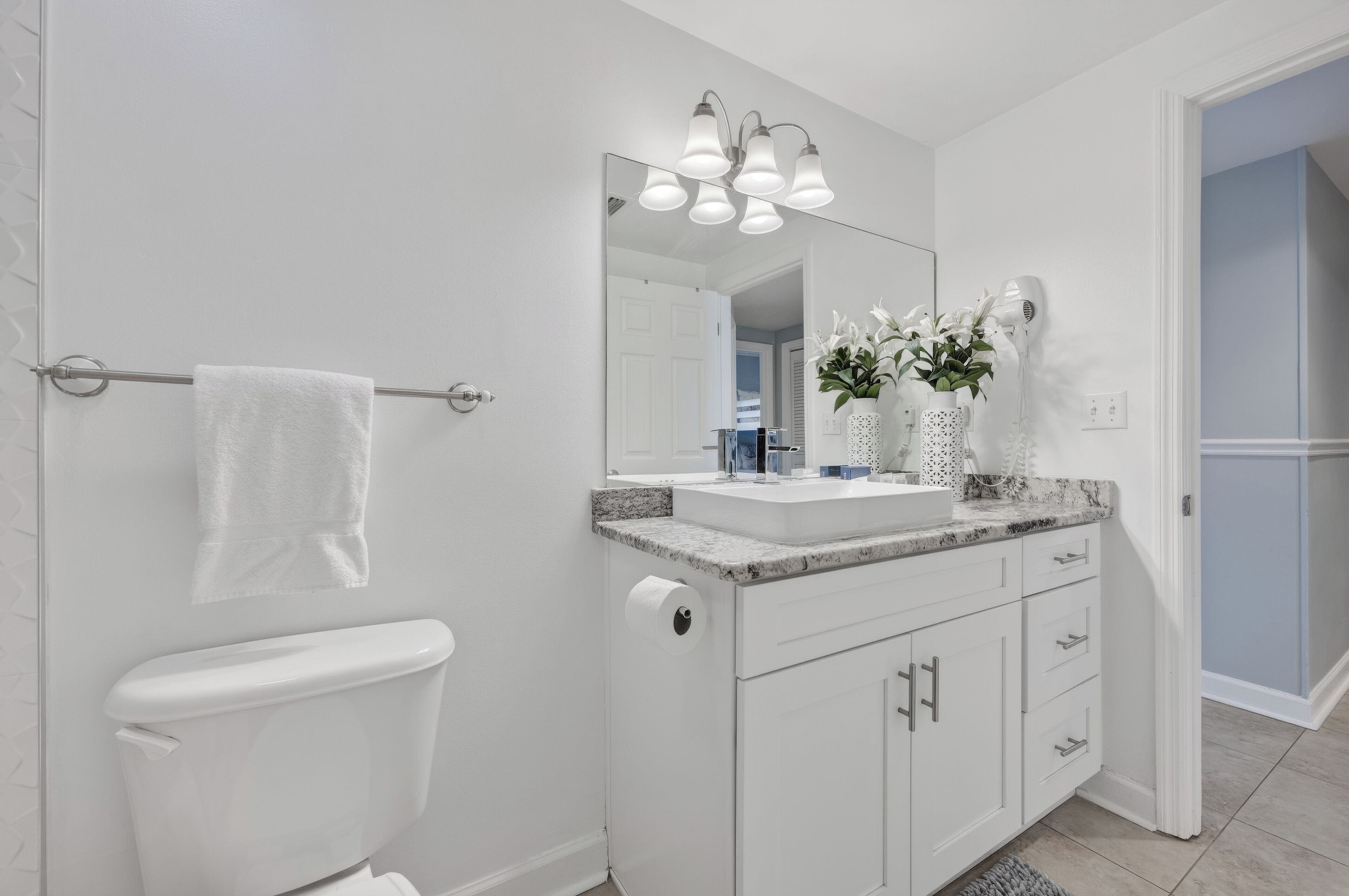 Une salle de bain moderne comprenant des toilettes, un lavabo avec un plan de travail en marbre, un miroir et un porte-serviettes.