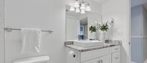 Une salle de bain moderne comprenant des toilettes, un lavabo avec un plan de travail en marbre, un miroir et un porte-serviettes.