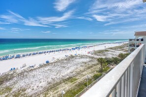 A beach view with a clear sky, a sandy beach, and a building with a balcony overlooking the beach.