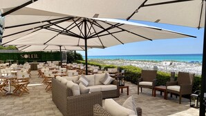 Un espace extérieur aménagé avec des meubles en osier et de grands parasols, offrant une vue sur la plage.
