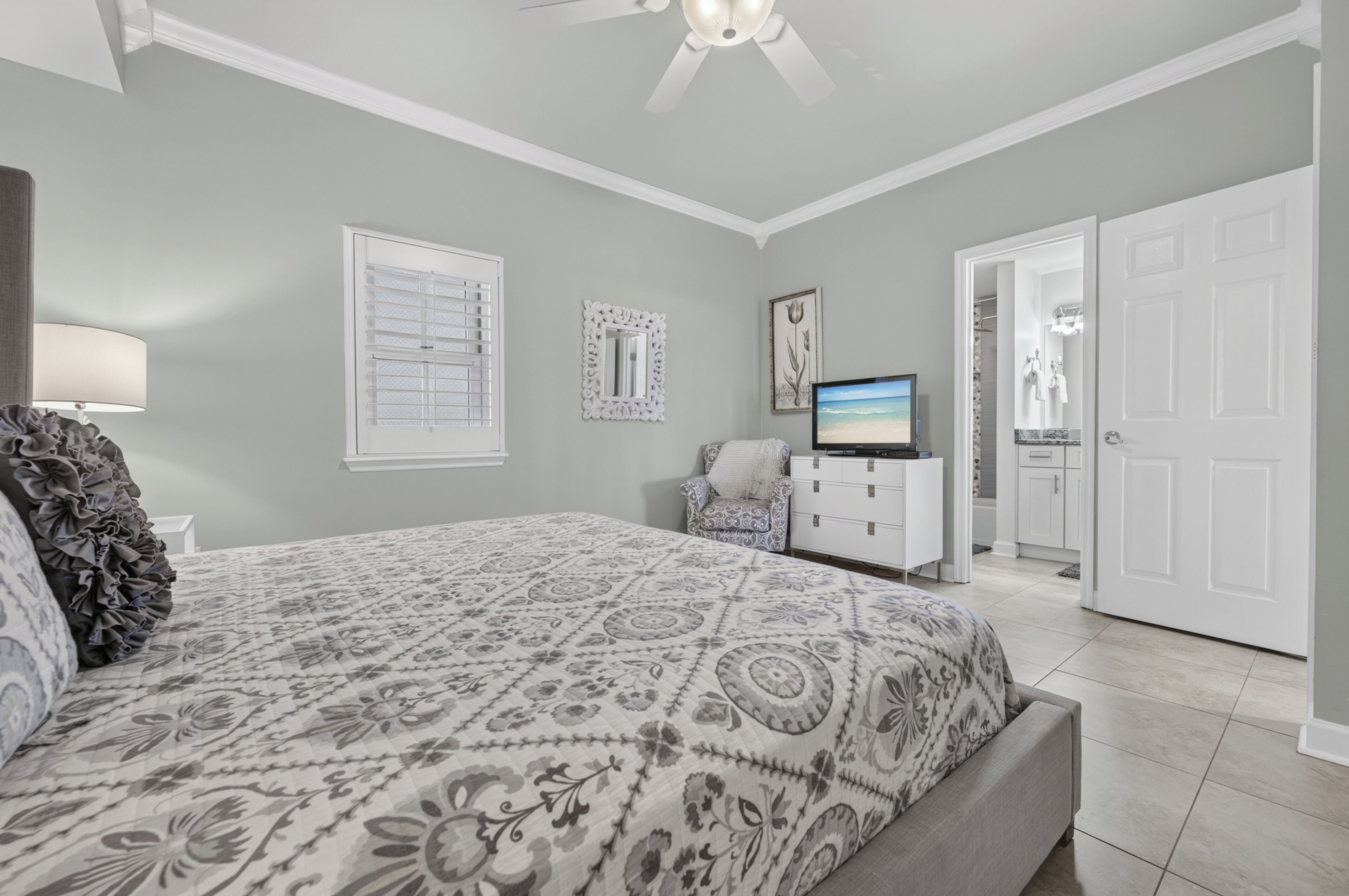 Un dormitorio con una cama, televisión, silla y puerta que da al baño.