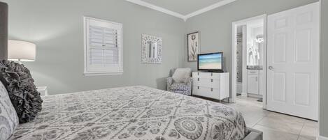 Un dormitorio con una cama, televisión, silla y puerta que da al baño.