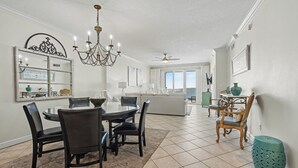 A spacious dining area with a round table, chairs, a chandelier, and a decorative mirror. - Inn at Crystal Beach 505 * Gulf Front with Beach Chair Set. Onsite dining! (Destin)