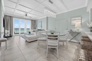 A spacious living area with a dining table, chairs, and a view of the ocean through large windows.