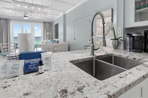 A modern kitchen with a marble countertop, stainless steel sink, and a chandelier.