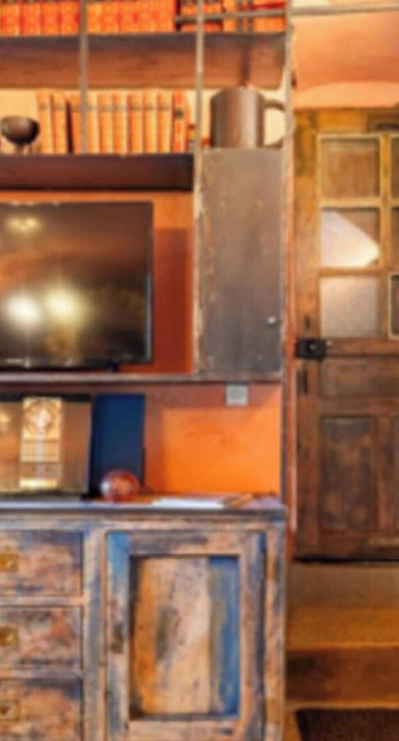 Une pièce avec un téléviseur posé sur un meuble en bois, une étagère remplie de livres et une porte dotée d’un panneau en verre.