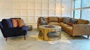 Un salon avec un fauteuil bleu foncé, un canapé marron clair et une table basse ronde en bois.