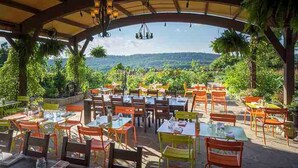 Un espace de restauration en plein air, avec des tables et des chaises, entouré d’une végétation luxuriante et offrant une vue sur un paysage montagneux.
