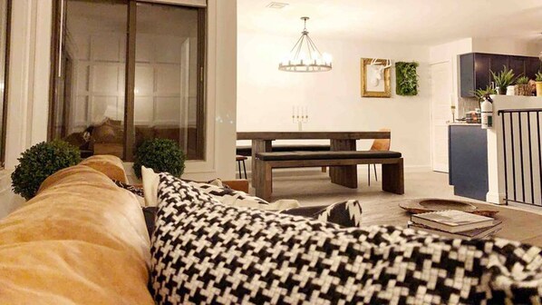 Un salon moderne avec un canapé, un banc et un coin repas agrémenté d’un lustre.