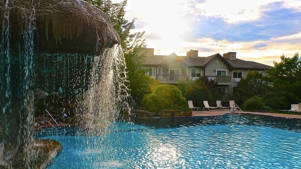 Une piscine agrémentée d’une cascade, entourée de chaises longues, avec une grande maison en arrière-plan.