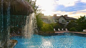 A swimming pool with a waterfall feature, surrounded by lounge chairs and a large house in the background. - Luxe 10 guest Cabin/Skiing/Pools/Tennis/Gym/Hiking (vernon)
