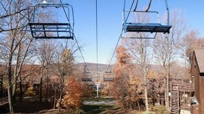 A ski lift with chairs suspended by cables, surrounded by trees with autumn foliage and a mountain in the background. - Luxe 10 guest Cabin/Skiing/Pools/Tennis/Gym/Hiking (vernon)