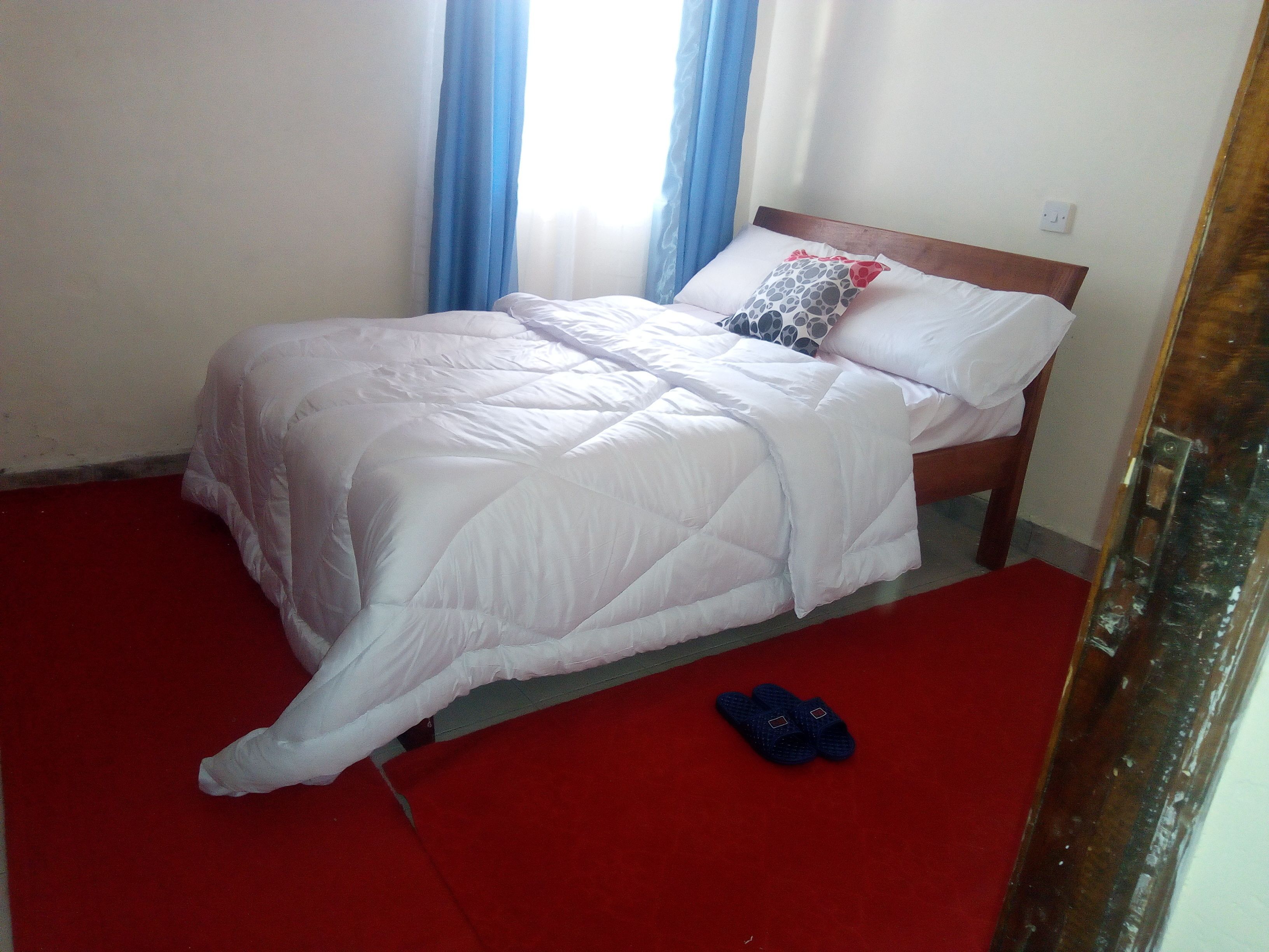 Una cama con edredón blanco, cabecero de madera y alfombra roja.