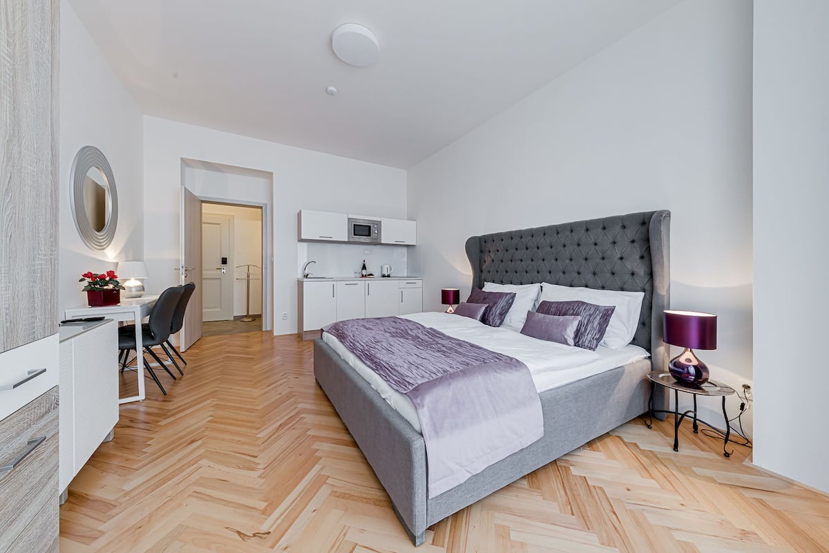 A modern bedroom with a large bed, a desk, and a kitchenette.