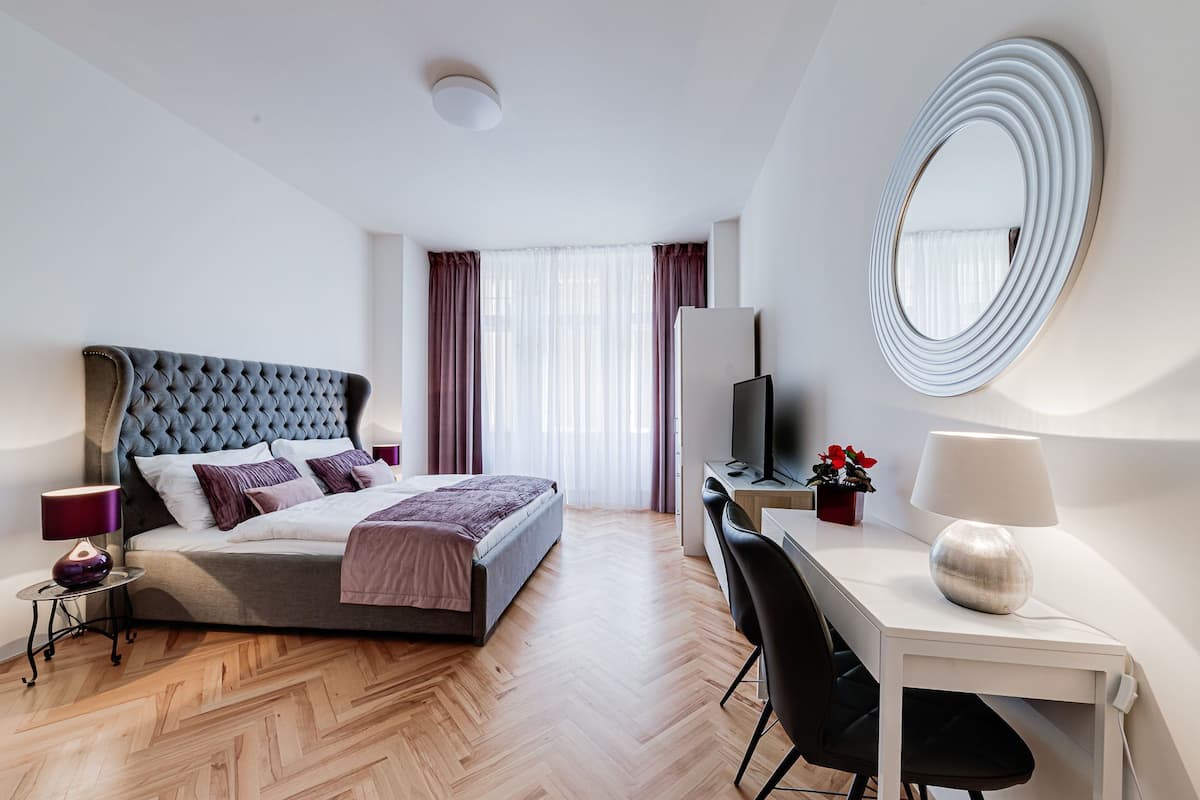 A modern hotel room with a large bed, a desk with a computer, a chair, and a mirror.