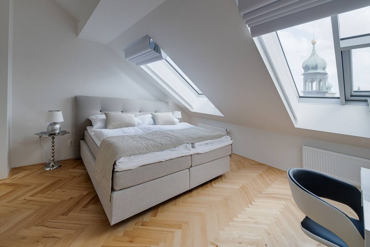 A bedroom with a bed, a chair, a lamp, and a skylight.