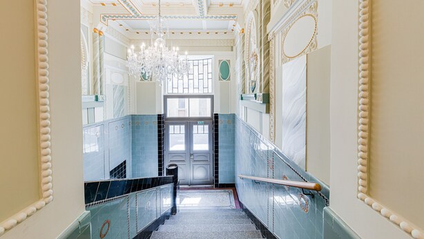 Un'ampia sala con un lampadario, soffitto decorato e una porta con la scritta 'EXIT'.