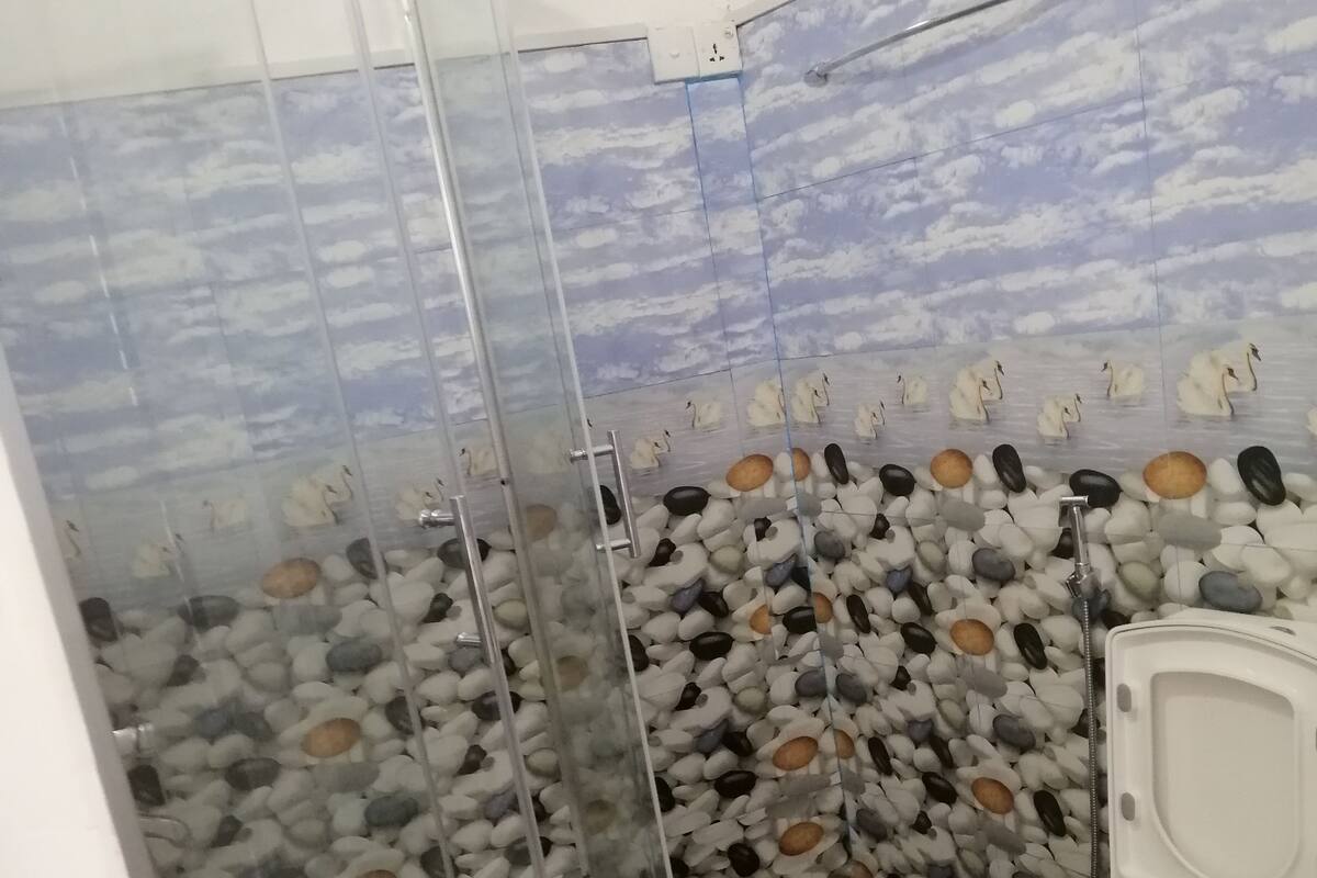A bathroom with a glass-enclosed shower, a toilet, and a wall decorated with a sky and water theme.