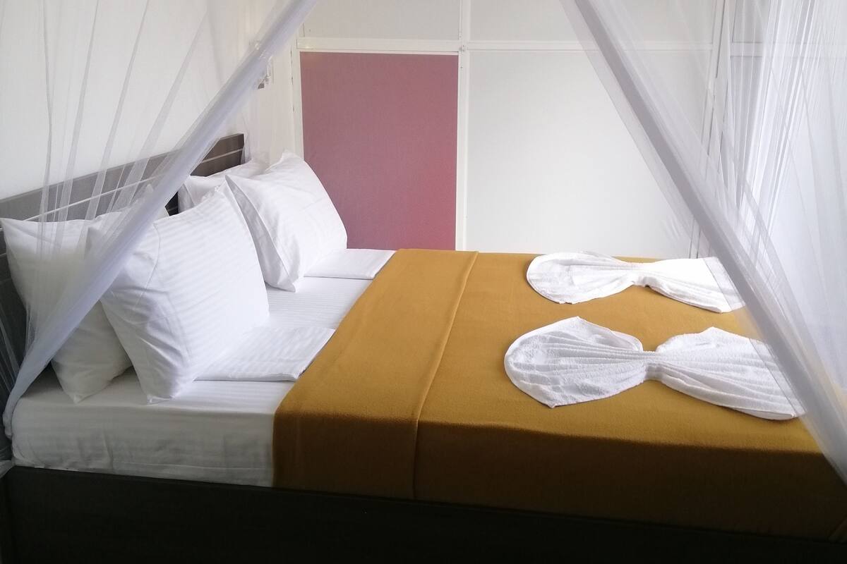 A bed with a white canopy, a mustard-colored bedspread, and white towels.
