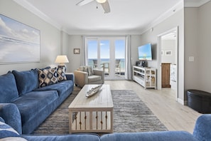 A living room with a sofa, coffee table, and TV, a balcony with a view, and a dining area.