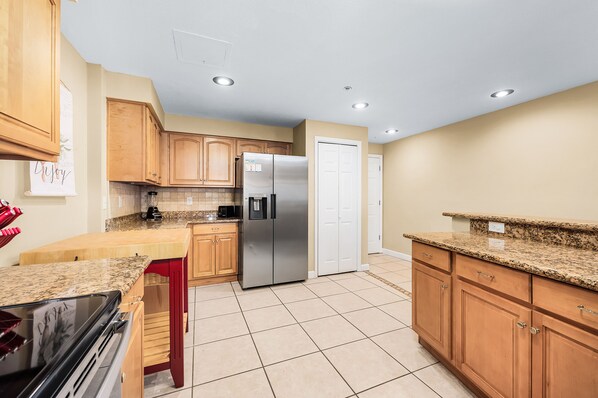 A kitchen with wooden cabinets, a stainless steel refrigerator, granite countertops, and a tiled floor.