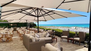 An outdoor seating area with wicker furniture and large umbrellas, overlooking a beach.