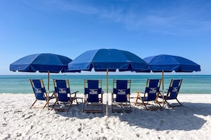 Una playa con cinco sillas azules y sombrillas dispuestas en fila frente al océano.