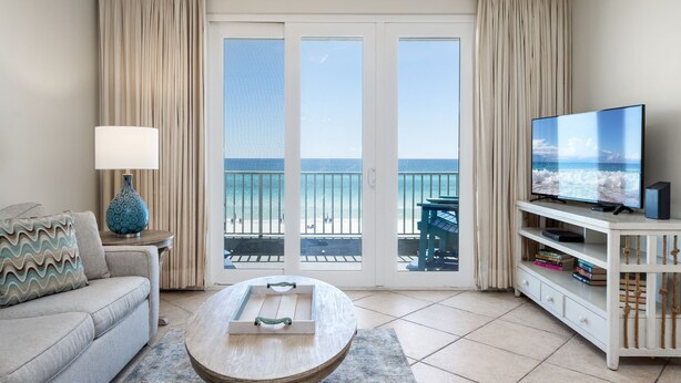 Una sala de estar con sofá, mesa de centro, televisión y un balcón con vista a la playa.