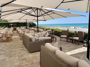 Un espacio de estar al aire libre con mobiliario de mimbre y sombrillas grandes, con vistas a una playa.