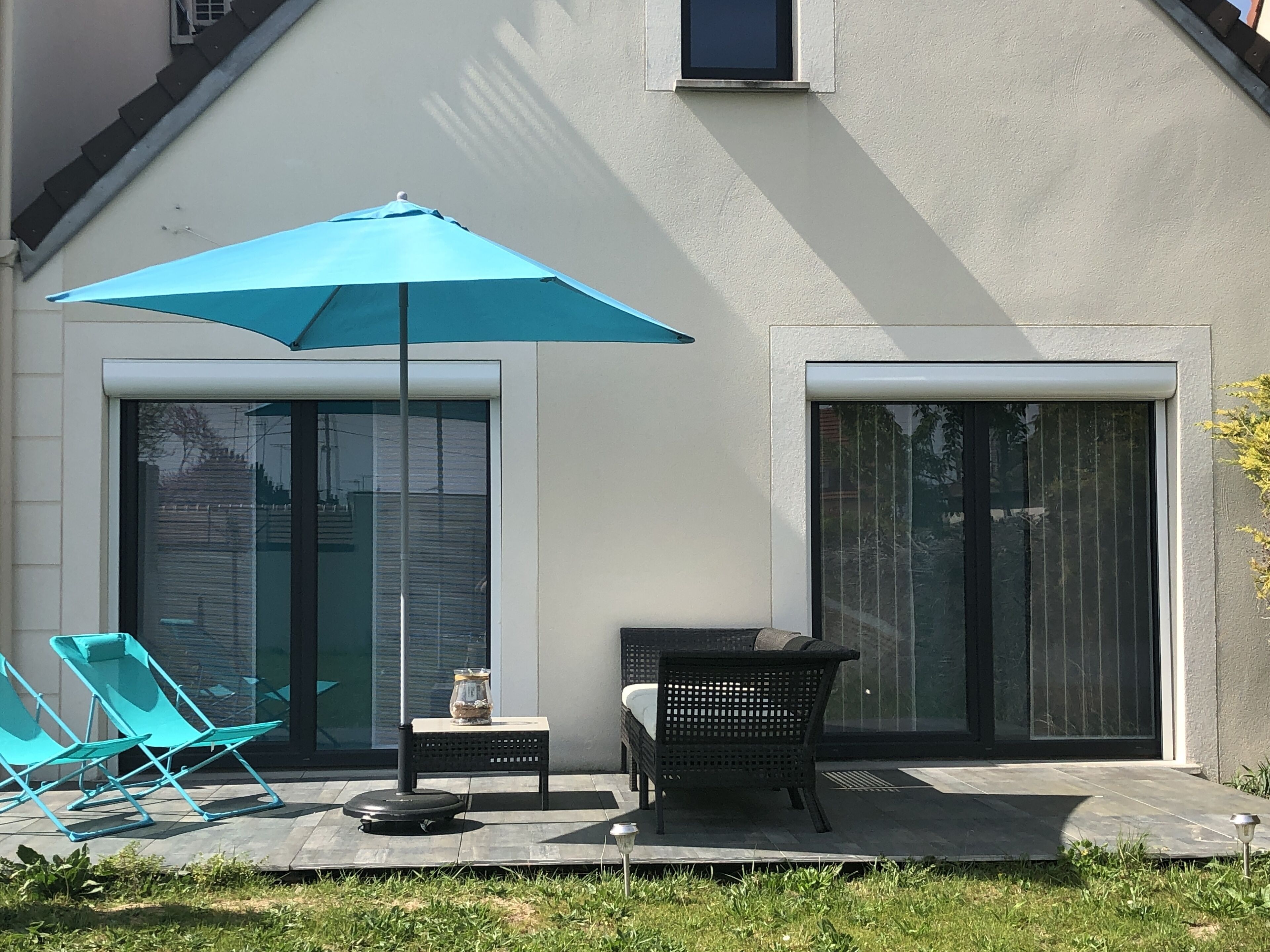 Un patio con mesa y sillas, una sombrilla azul y una pequeña mesa con un adorno.