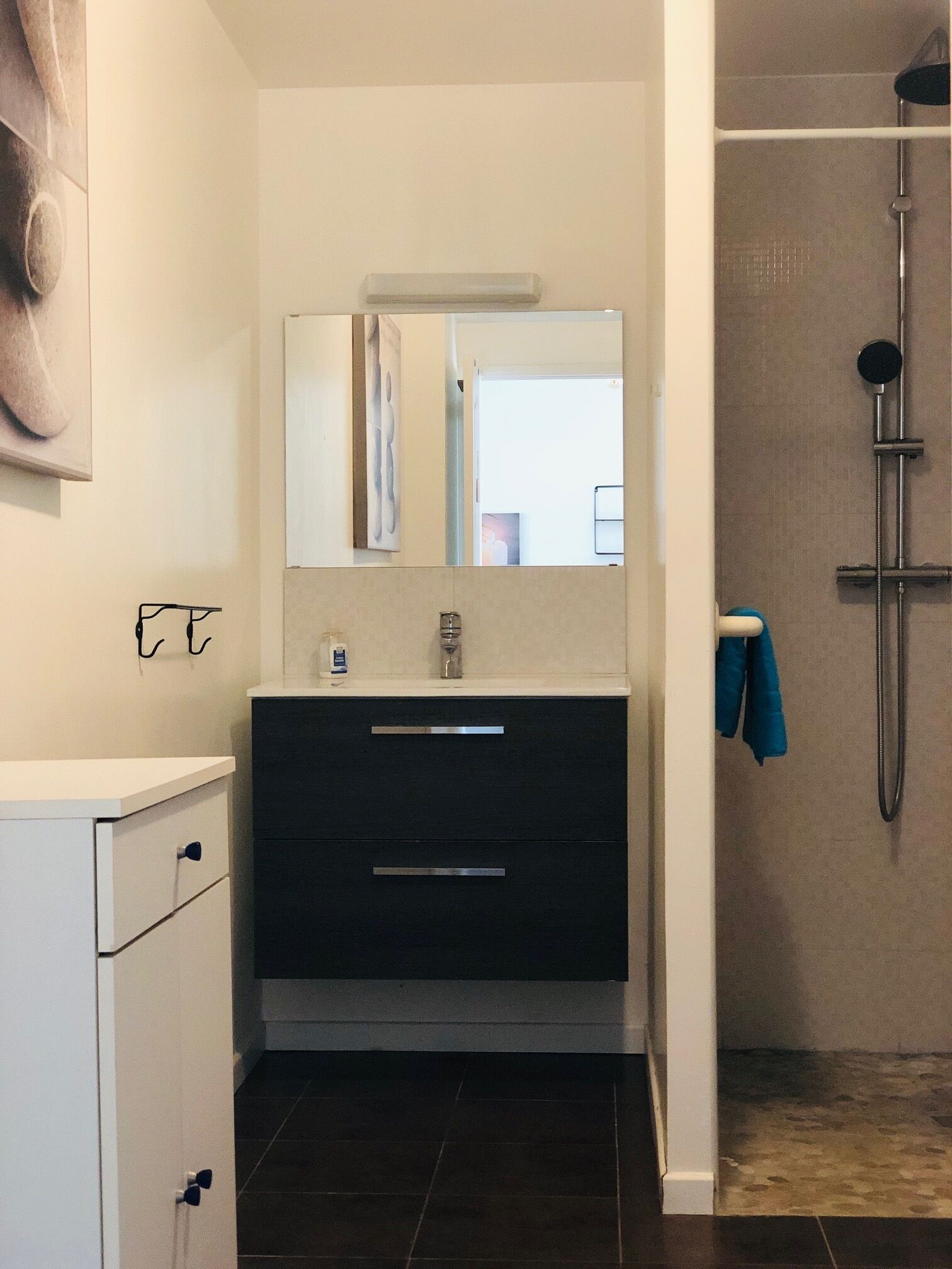 A modern bathroom with a white vanity, dark drawers, a mirror, and a shower area.