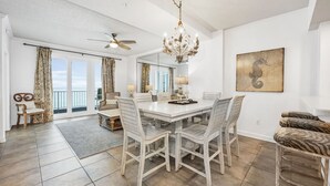 Un comedor amplio con una mesa y sillas blancas, una araña y un gran ventanal con cortinas.