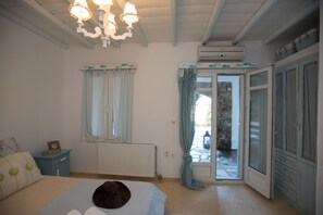 Une chambre à coucher comprenant un lit, une table de chevet, une fenêtre avec des rideaux, un appareil de climatisation et une porte donnant sur l’extérieur.