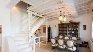 A dining area with a wooden table and chairs, a staircase, and a bookshelf with various items. - Beautiful Villa at Panormos (Mykonos)
