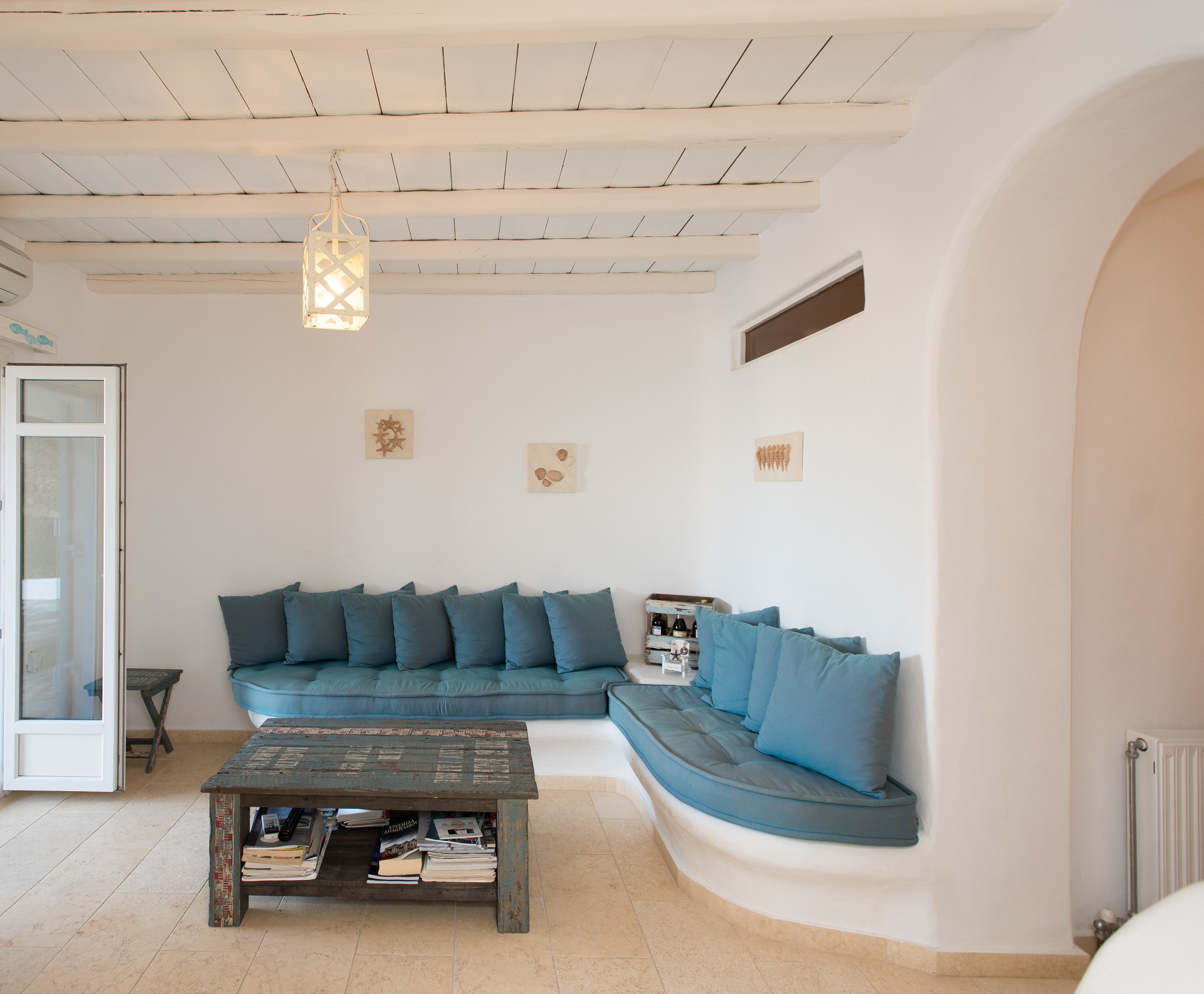 A living room with a curved sofa, a coffee table with books, and a hanging light fixture.