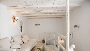 A white room with a wooden ceiling, a white sofa, a small table, and a staircase. - Beautiful Villa at Panormos (Mykonos)