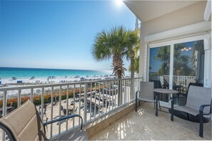 A balcony with a view of the beach, outdoor seating, and a palm tree. - Inn at Crystal Beach 203 * Gulf Front with Beach Chair Set. Onsite dining! (Destin)