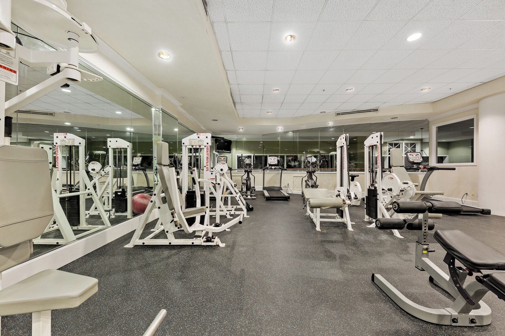 Ein Fitnessstudio mit unterschiedlichen Trainingsgeräten, Spiegeln und einem Teppichboden.
