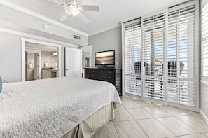 A bedroom with a bed, a television, a ceiling fan, and a view through a window with blinds. - Inn at Crystal Beach 404 * Gulf Front with Beach Chair Set. Onsite dining! (Destin)