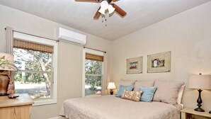 A bedroom with a large bed, two windows with blinds, a ceiling fan, and a bedside table with a lamp. - Texas Sage I Cabin close to the Square! (Wimberley)