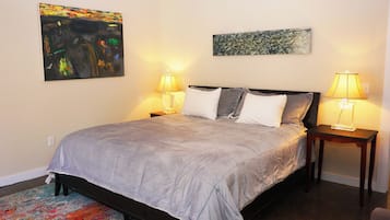 A neatly made bed with a grey duvet, two bedside lamps, and two paintings on the wall.