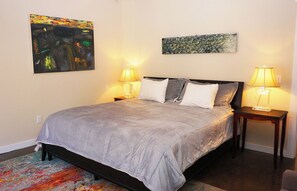A neatly made bed with a grey duvet, two bedside lamps, and two paintings on the wall.