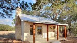 A small stone cabin with a porch, surrounded by trees and a grassy field. - Texas Sage I Cabin close to the Square! (Wimberley)