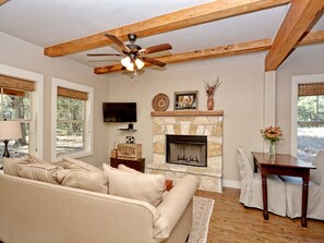 A living room with a stone fireplace, a ceiling fan, a television, and a dining area with a table and chairs. - Texas Sage I Cabin close to the Square! (Wimberley)