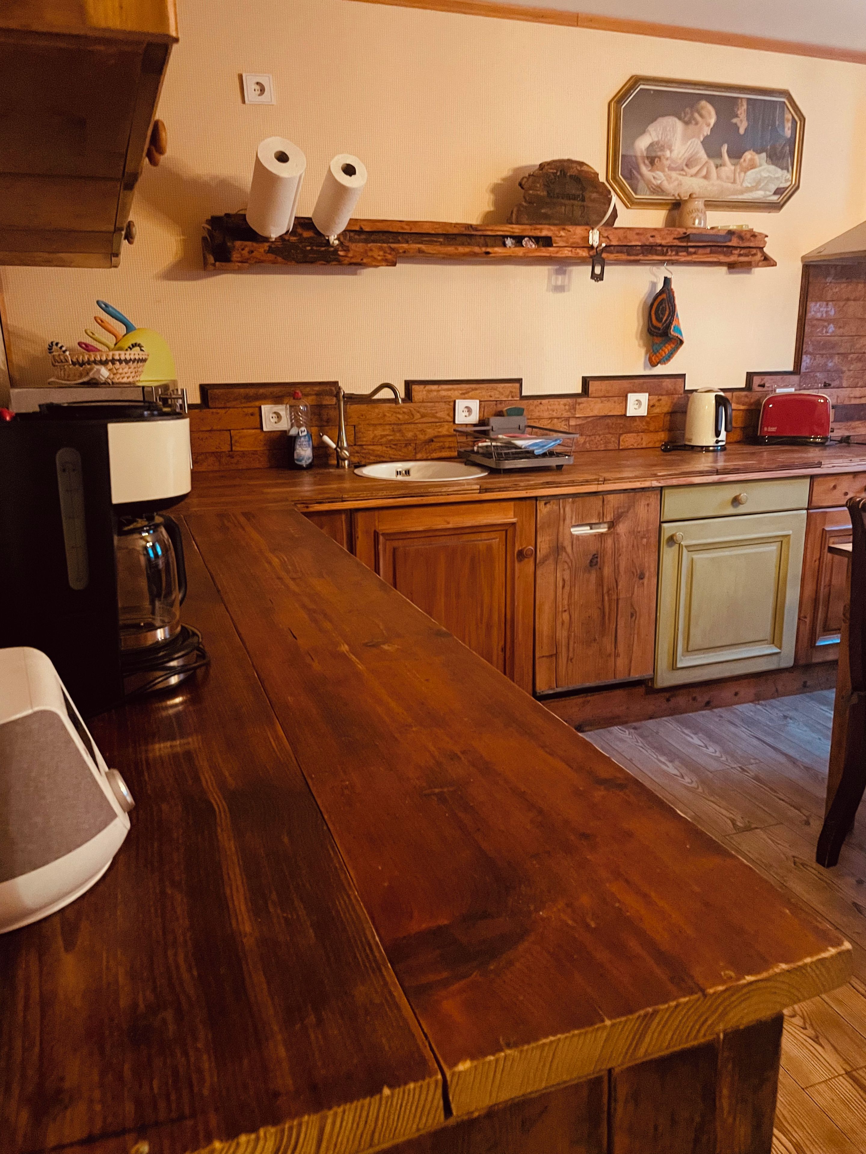 Une cuisine avec des meubles de rangement en bois, un long plan de travail, un évier et une machine à café.