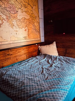 Een bed met een bekleedsel in blauw-wit patroon, een kussen en een grote kaart aan de muur.