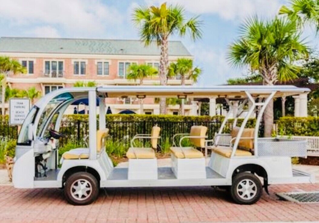 Un carrito de golf blanco con asientos color beige estacionado frente a un edificio de techo verde y palmeras.