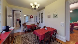 A dining area with a red tablecloth, wooden chairs, a chandelier, and a patterned rug. - Romantic Dogwood Room, Clawfoot Bathtub in Historic Hyde House, Hocking Hills (Nelsonville)