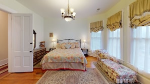 A bedroom with a large bed, a bench, a chandelier, and curtains. - Romantic Dogwood Room, Clawfoot Bathtub in Historic Hyde House, Hocking Hills (Nelsonville)