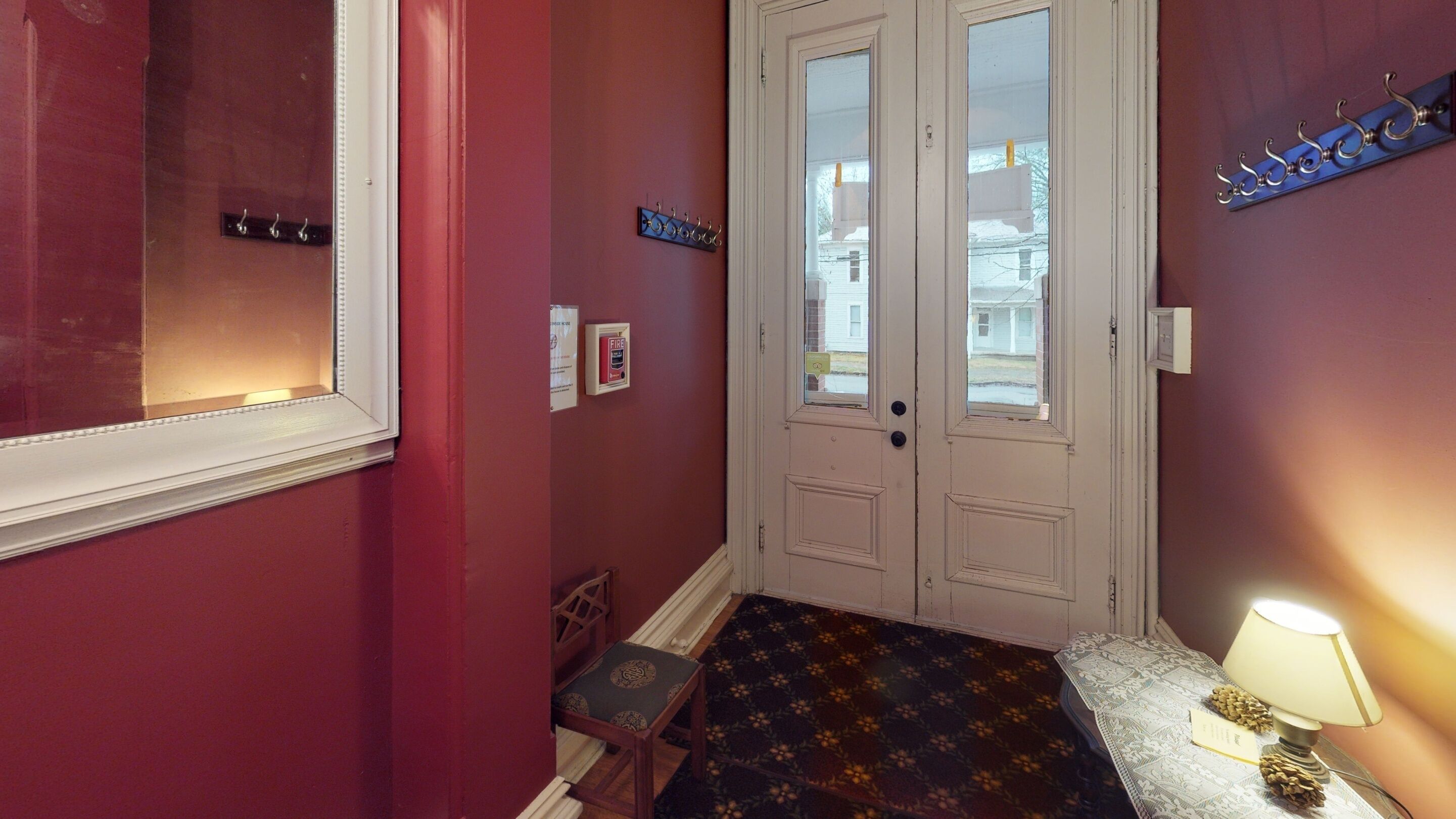 A hallway with a double door, a small bench, a patterned rug, a coat rack, and a wall-mounted fire alarm.